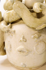 Close-up of a sculptural ceramic vessel with organic, abstract forms and a glossy cream glaze, showing textured surfaces and rounded protrusions.