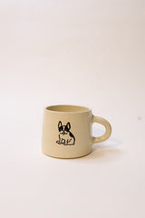 A beige ceramic coffee mug with a black line art illustration of a French Bulldog on the front, set against a plain off-white background.