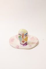 Back of small ceramic incense holder with hand painted face design on a white background