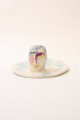 Back of small ceramic incense holder with hand painted face design on a white background