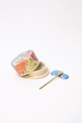 A colorful ceramic butter dish with wooden spreader and ceramic spreader rest