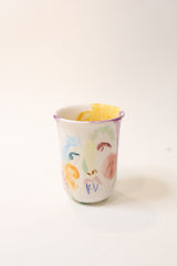 Ceramic mug with colorful hand painted face design on a white background