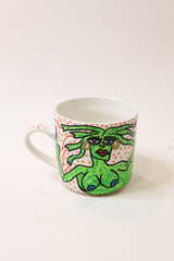 A white ceramic coffee mug featuring a hand-drawn green female figure with red lips and a red-and-white polka dot pattern on the side, set against a plain white background.