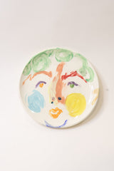 Round ceramic plate with colorful abstract face on a white background