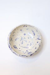 A round ceramic bowl with a cream-colored interior decorated with blue abstract scribbles and patterns, shown from a top-down view on a white background.