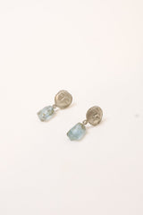 A pair of dangle earrings featuring round silver-toned faces, suspended from small links and hanging from aquamarine crystals, shown on a plain white background.