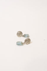 A pair of small dangle earrings with round silver-toned coin-like studs and light blue rectangular crystal drops, shown on a plain white background.