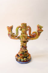 An ornate, multi-armed ceramic candelabra with a highly textured, organic sculptural design, covered in a multicolored glaze of green, orange, yellow, and brown, set against a plain white background.