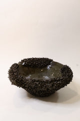 A dark brown textured decorative object with a glossy center, photographed against a plain off-white background.