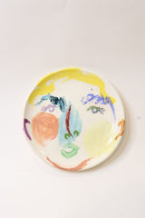 Round ceramic plate with colorful abstract face on a white background